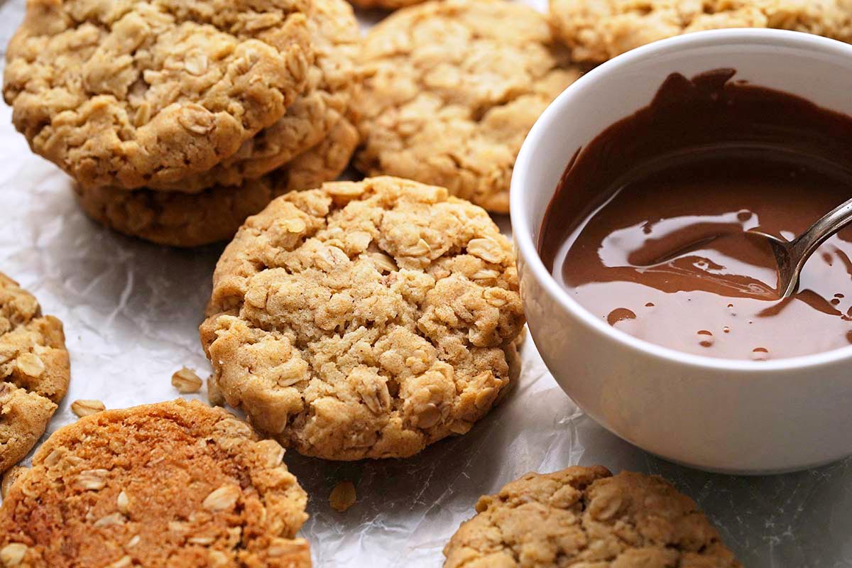 pile of crunchy oat biscuits next to bowl of melted chocolate