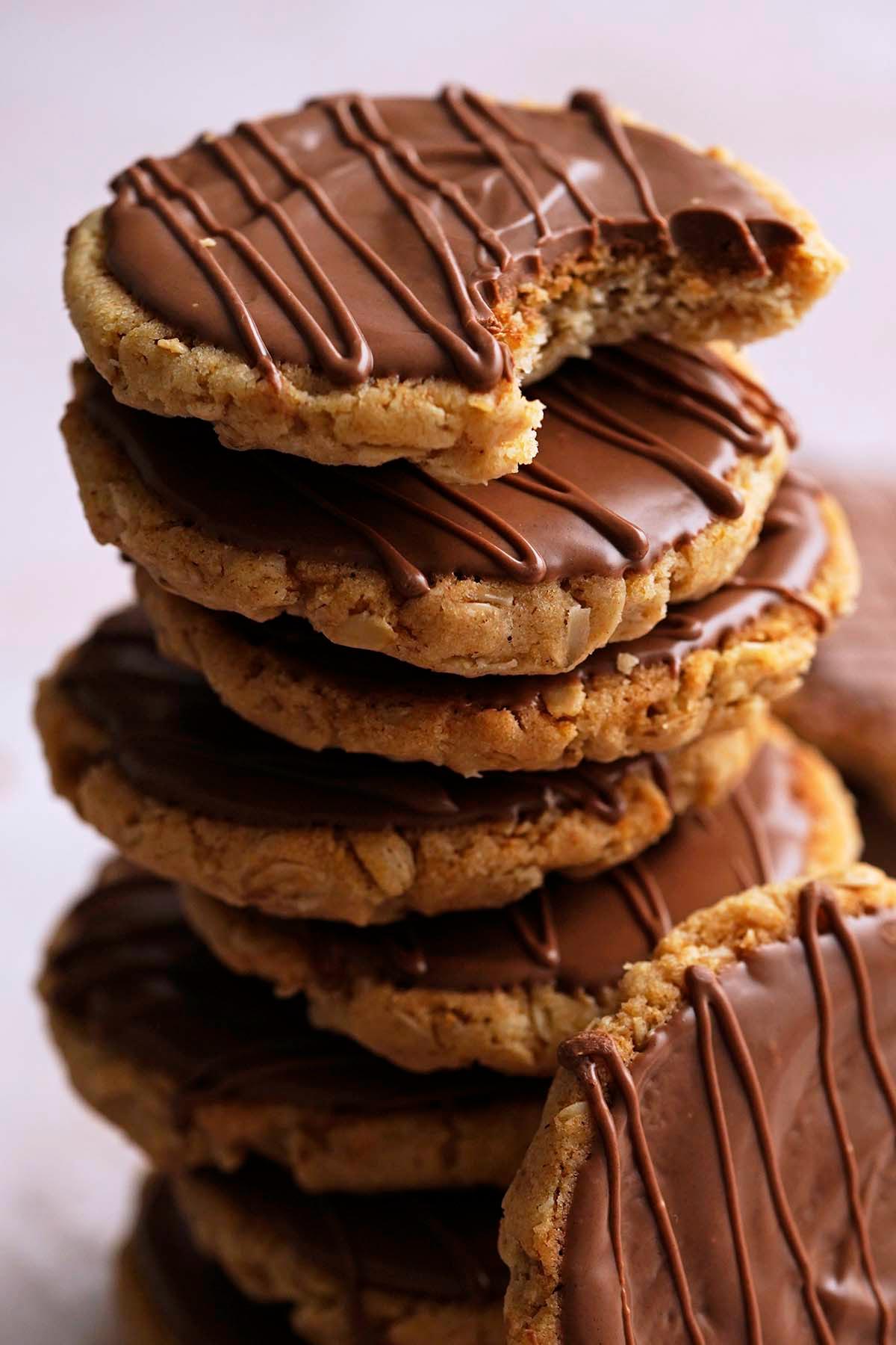 stack of crunchy oat cookies with chocolate topping with bite taken out of top cookie to show texture
