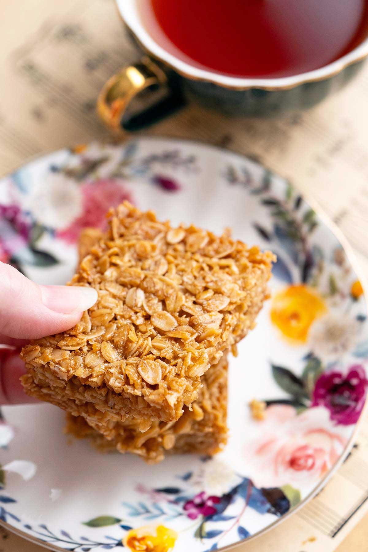 fingers picking up classic British flapjack from flowered plate with tea in the background