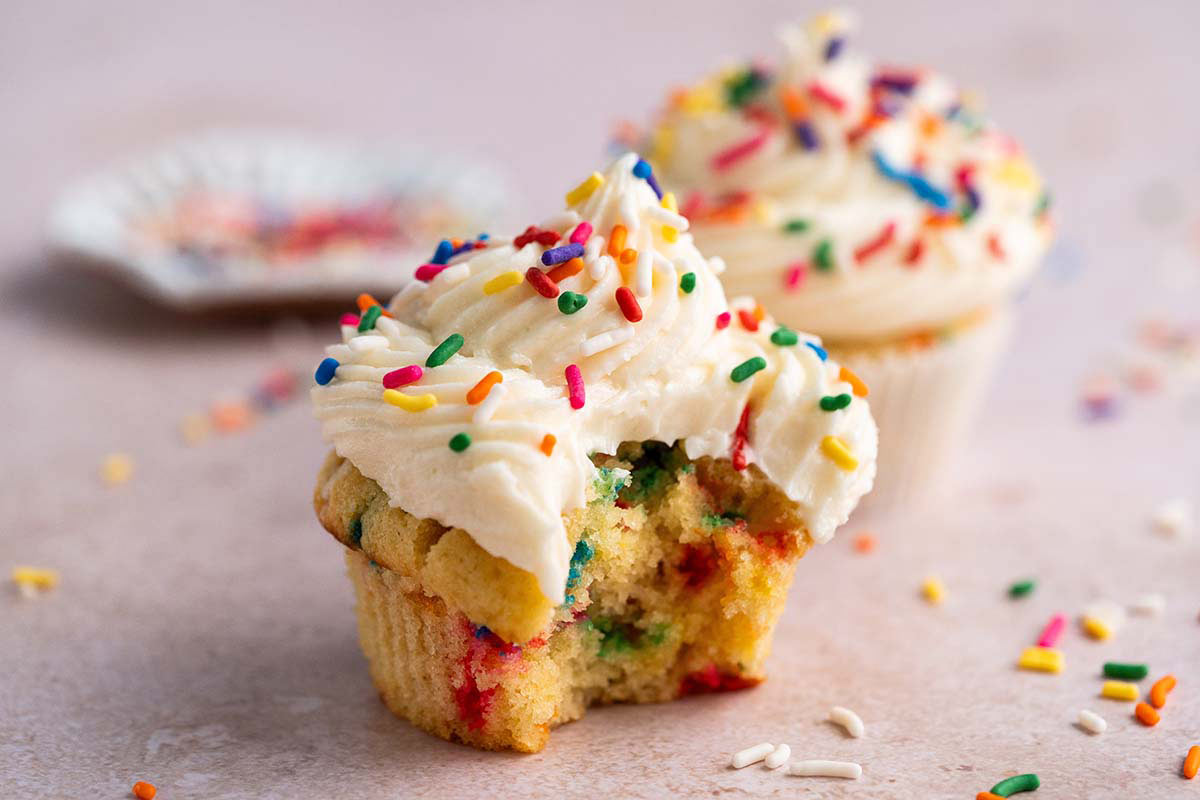 front view of 2 birthday funfetti cupcakes with bite out of one to show moist yellow cake
