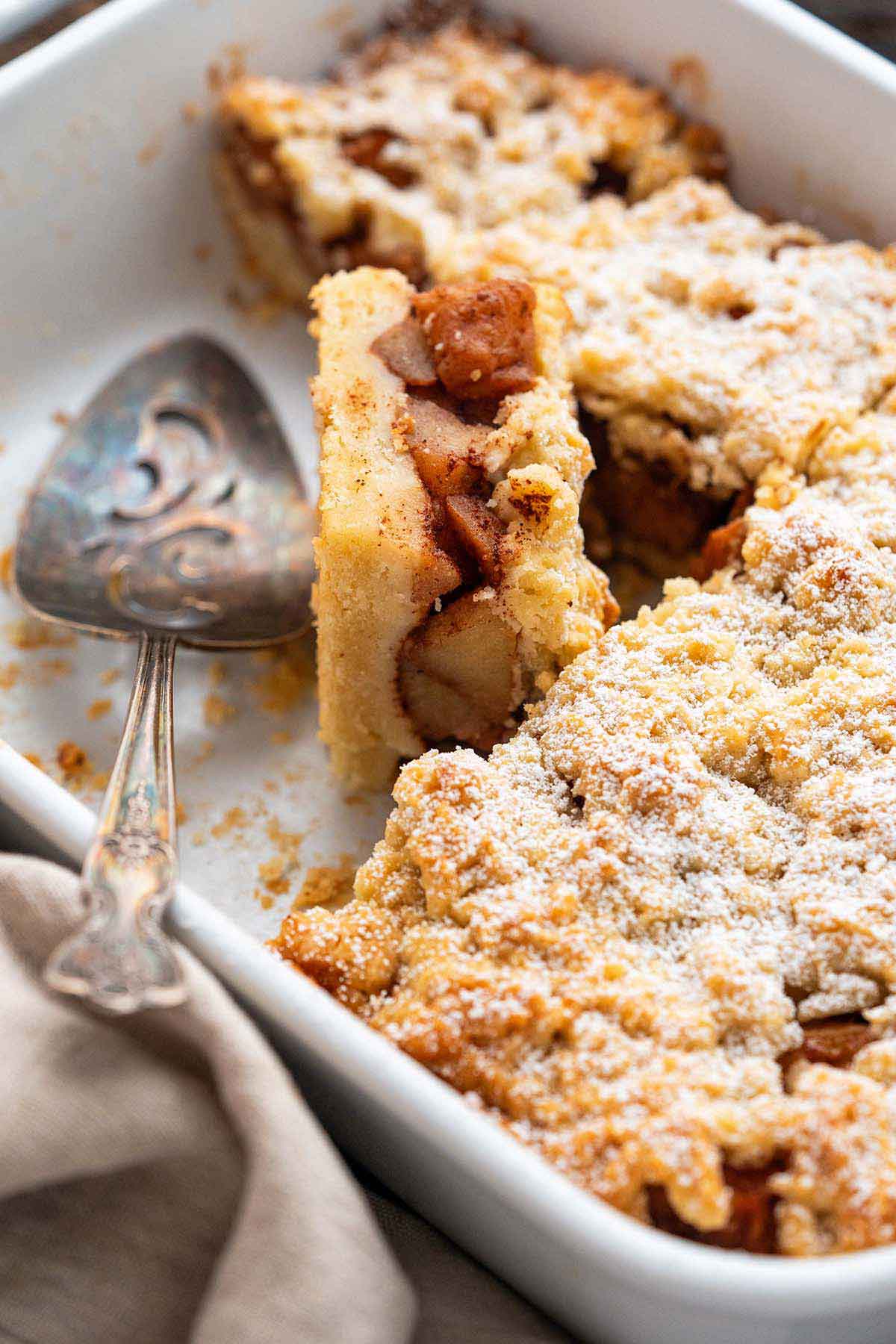 szarlotka in white staub casserole dish with one piece on its side to show apple filling