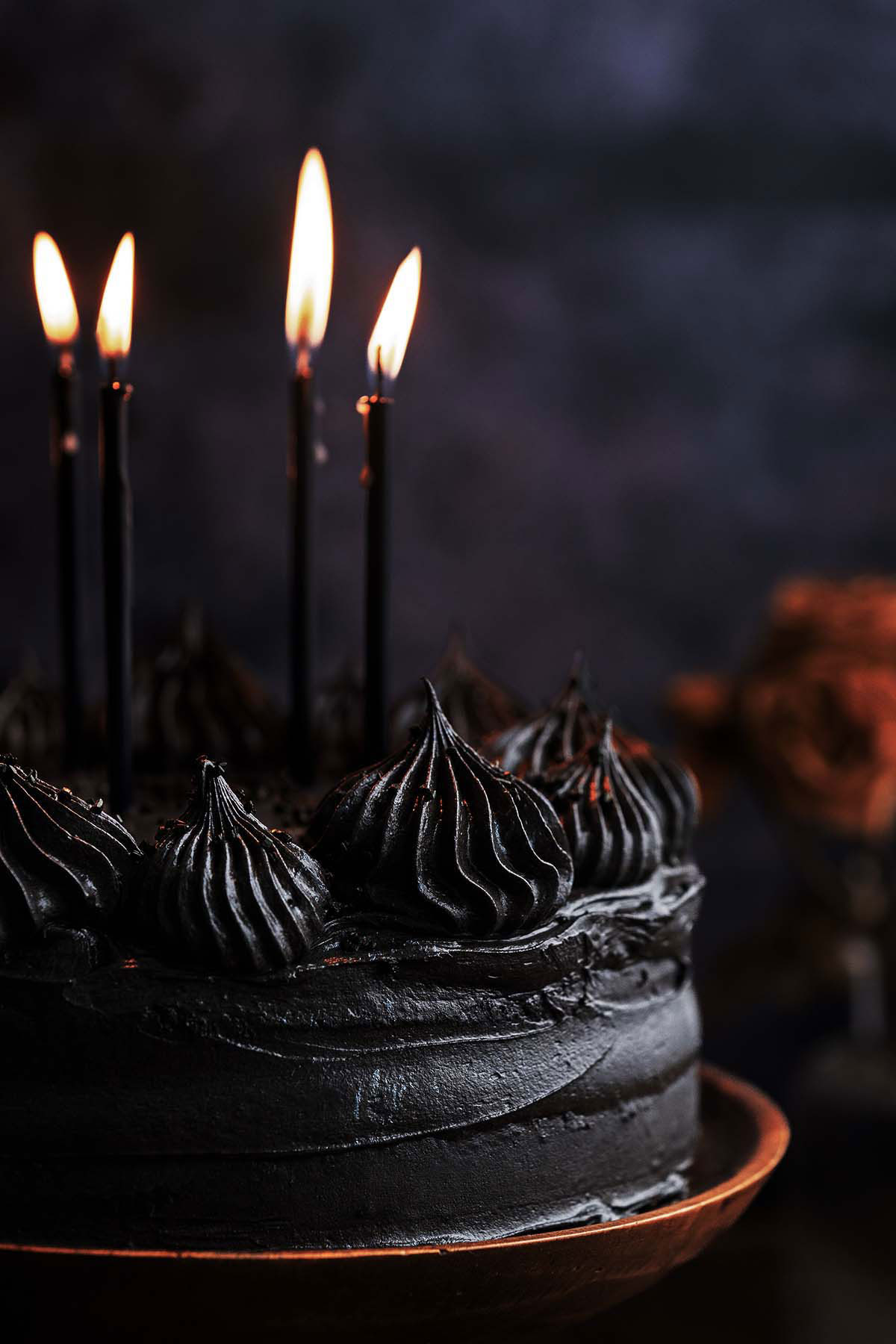 close up front view of black chocolate velvet cake with black frosting with lit candles on top
