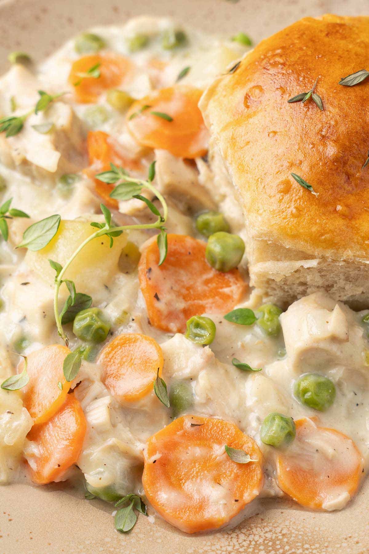 close up of creamy chicken casserole filling on plate topped with golden biscuit