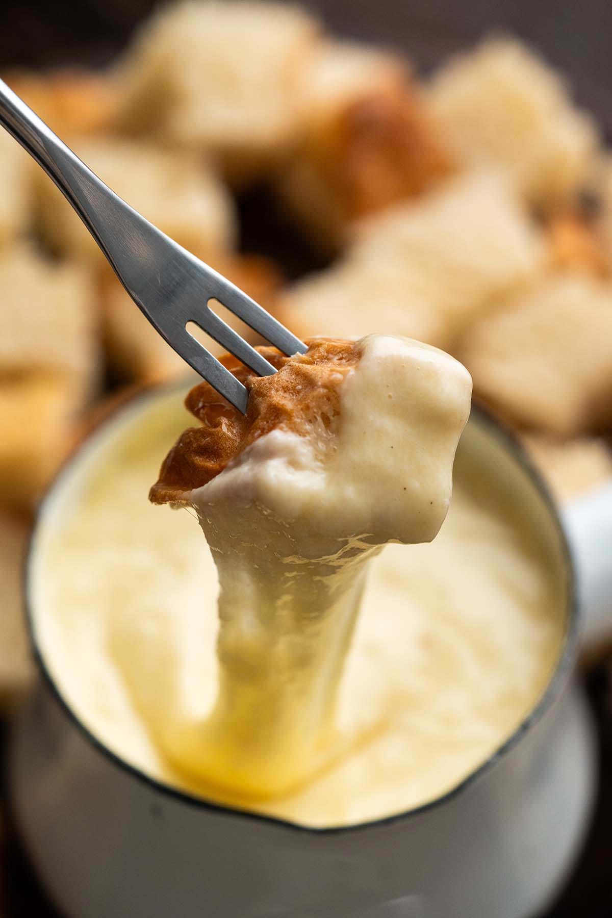 fondue fork with bread dipping into cheese fondue