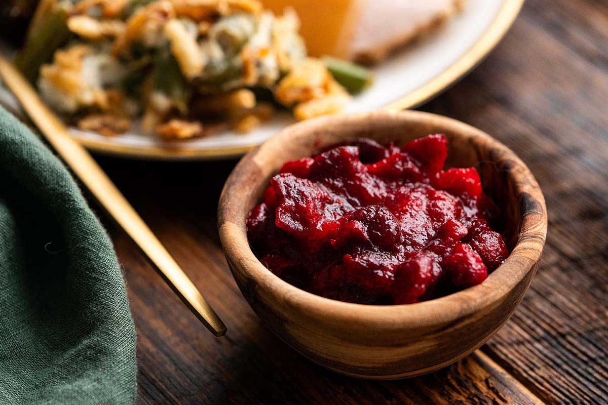 easy cranberry sauce in wooden bowl next to green linen on rustic wood table