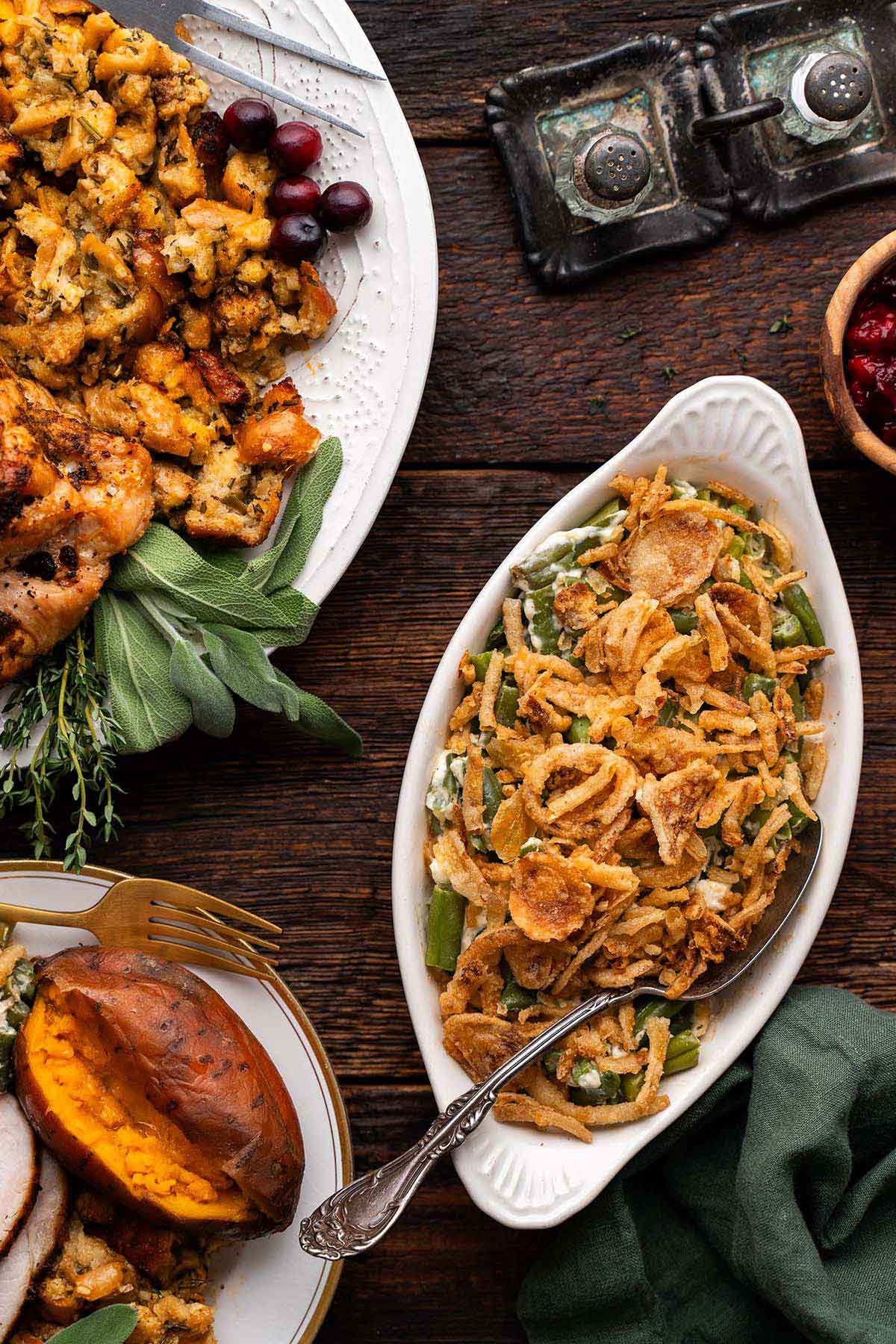 holiday green bean casserole in gratin dish on rustic wooden table with turkey dinner items