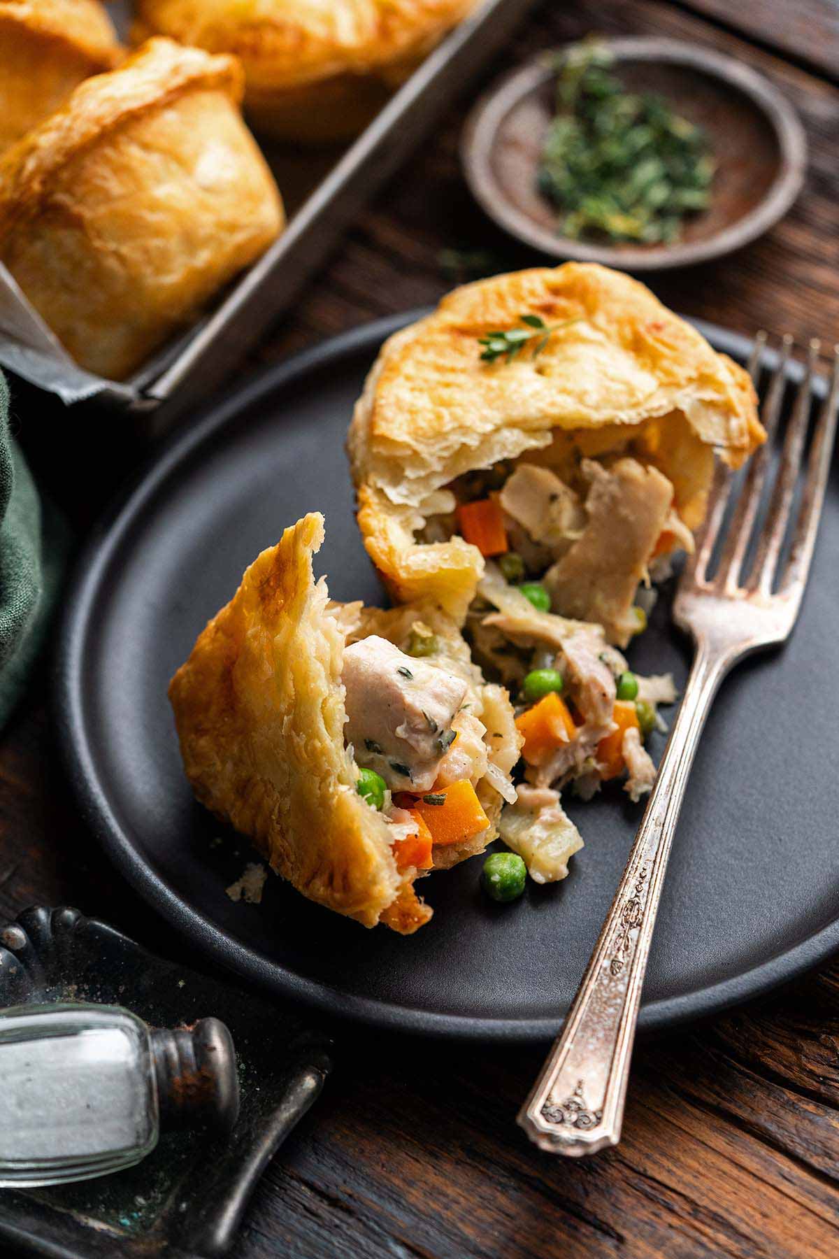 muffin tin chicken pot pie on black plate split open to show filling and flaky crust