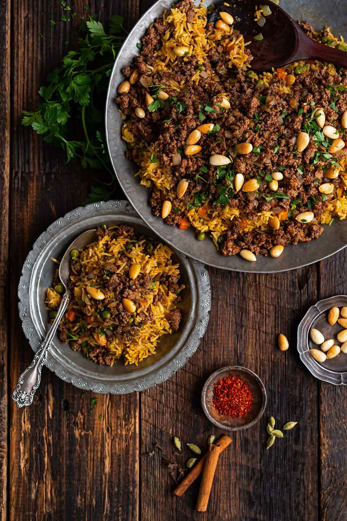 top view of large serving platter with lamb oozi rice with side dish next to it on rustic wood table