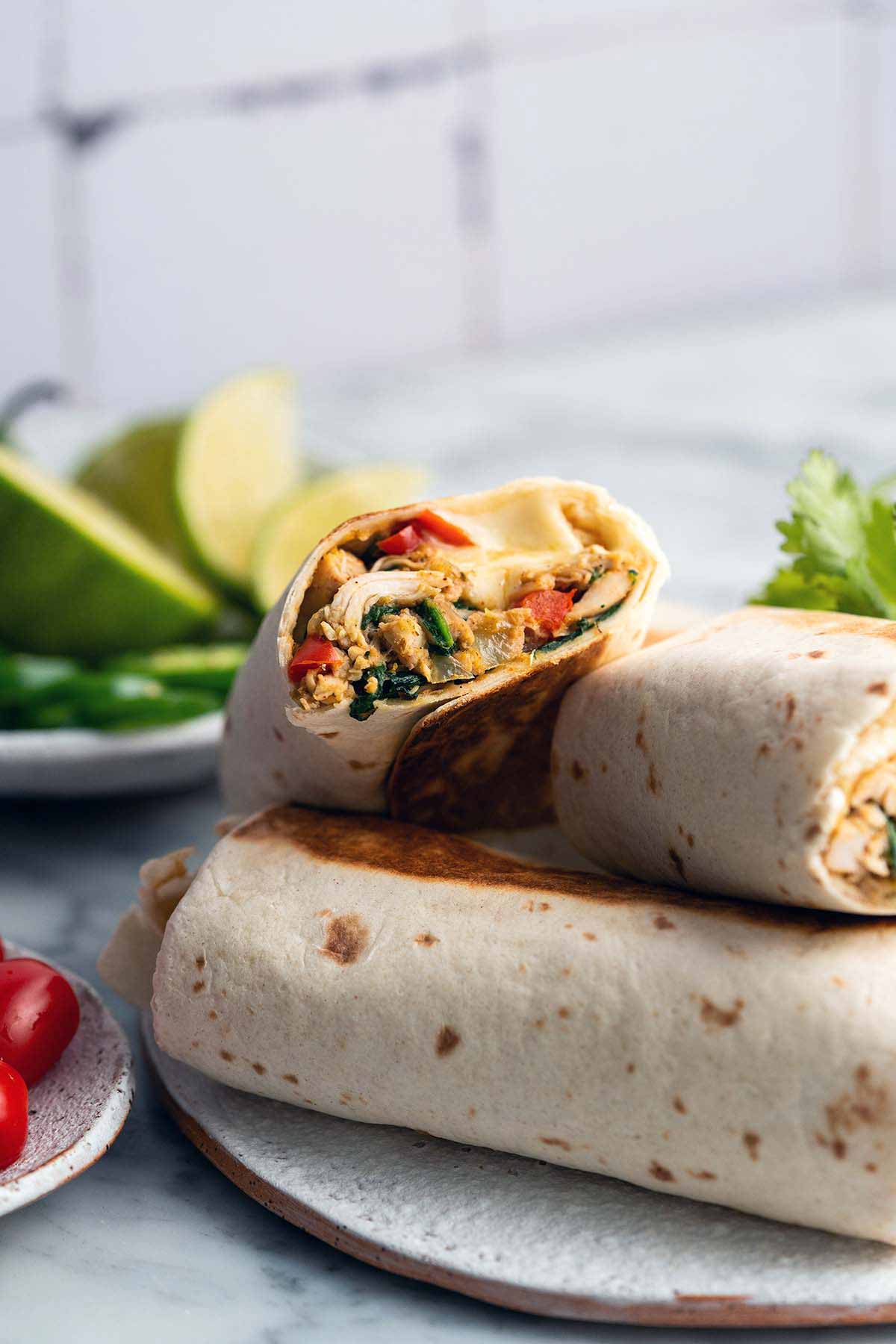 front view of plate of meal prep burritos with one cut in half to show chicken and cheese filling