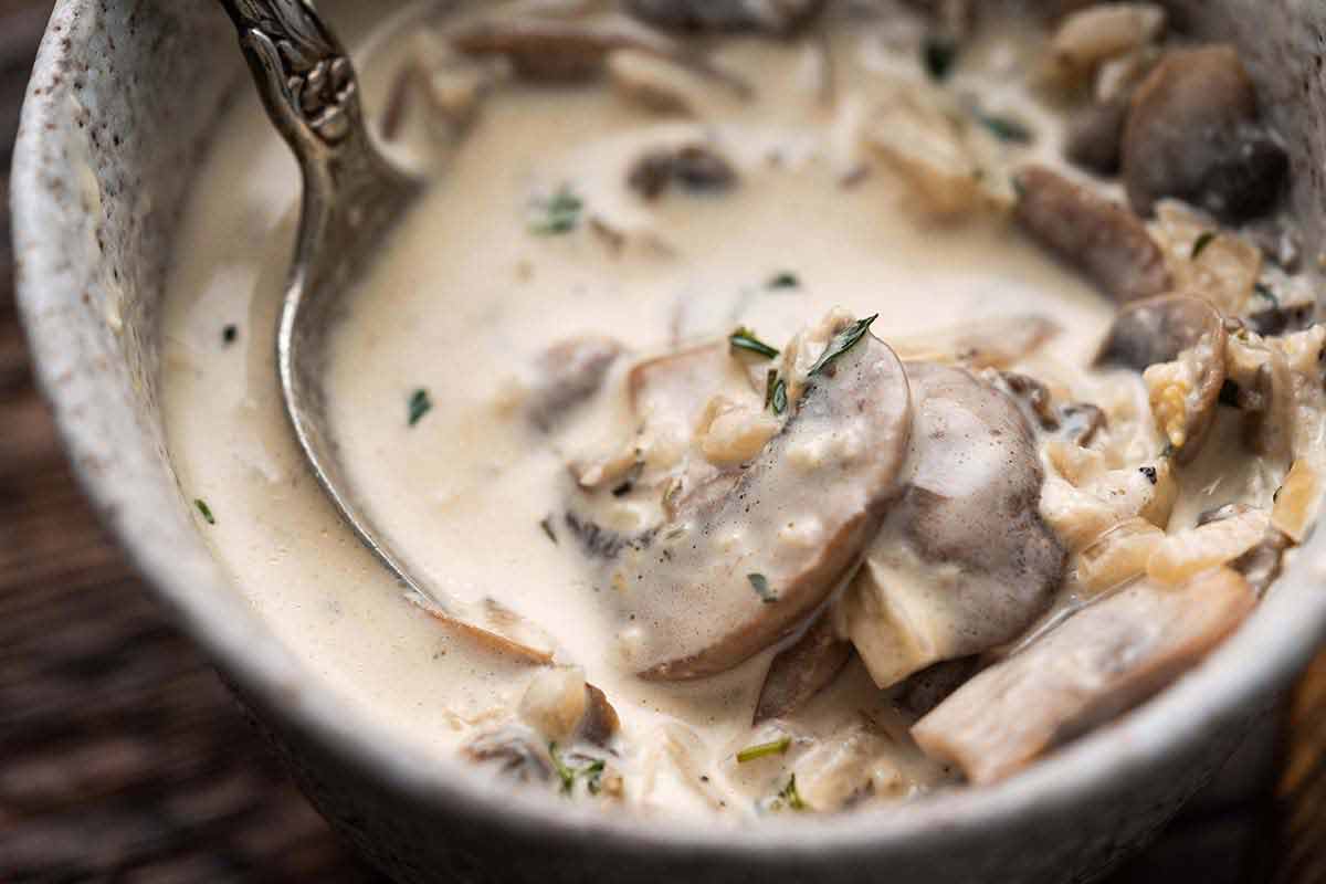close up of white wine and mushroom sauce with garlic and herbs in stoneware bowl