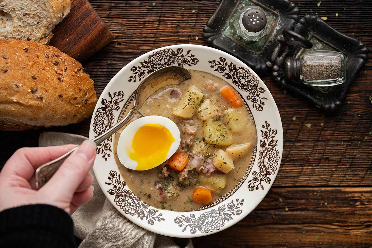 hand holding vintage spoon over vintage bowl of sour rye soup on rustic table
