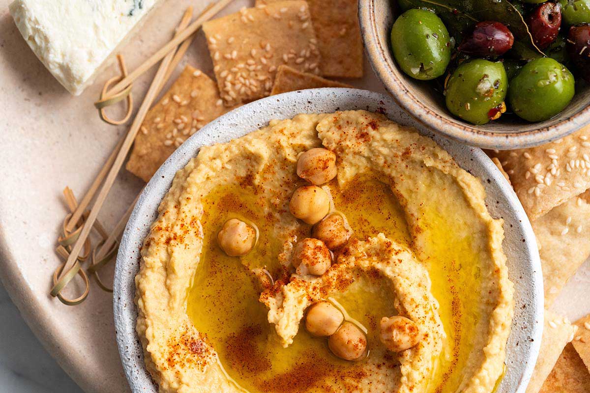 homemade garlic hummus next to blue cheese olives and crackers on platter