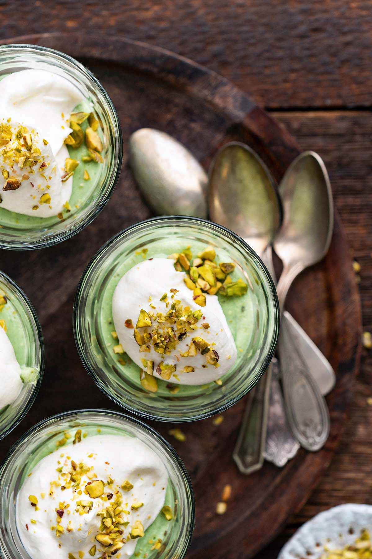 overhead view of homemade pudding in individual glasses topped with whipped cream and nuts