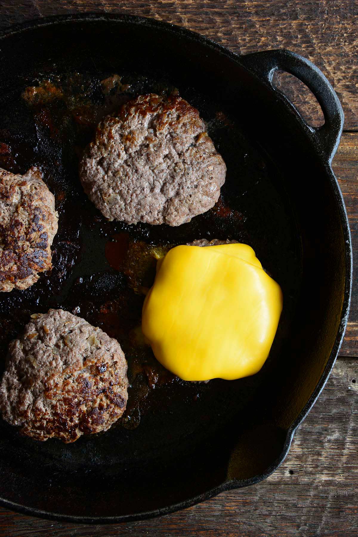 burgers cooked in a cast iron skillet with cheese on top of one