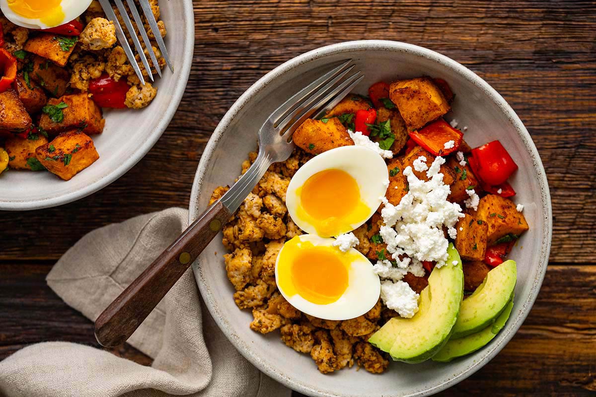 top view of nourishing breakfast bowl with potato hash sausage and eggs on wooden table