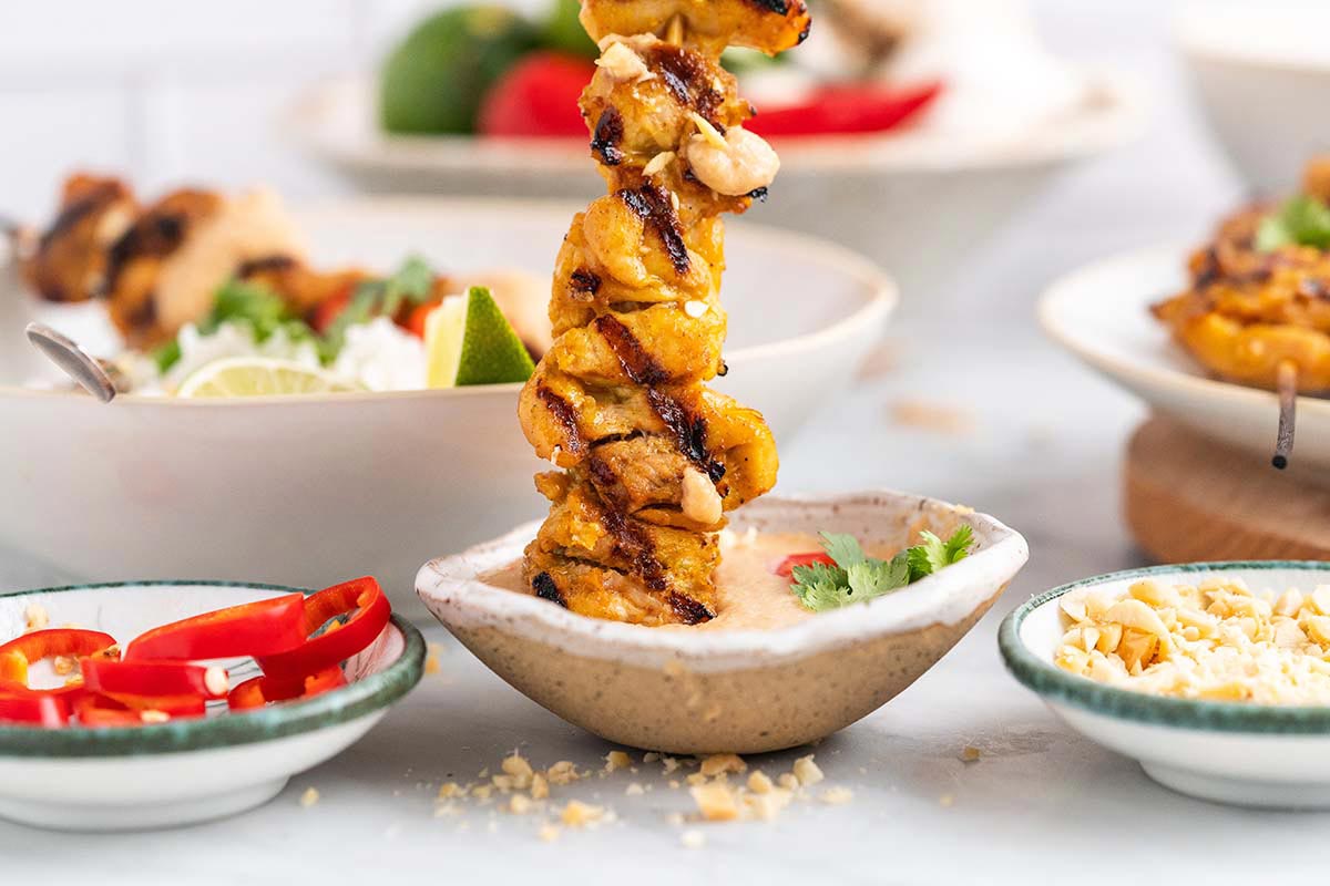 dipping grilled chicken skewer into peanut satay sauce