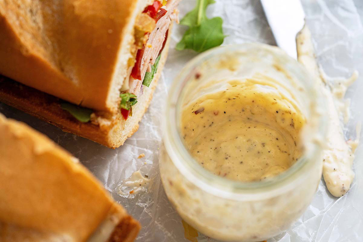 creamy tangy mayo sub sauce in glass jar next to Italian deli meat sandwiches