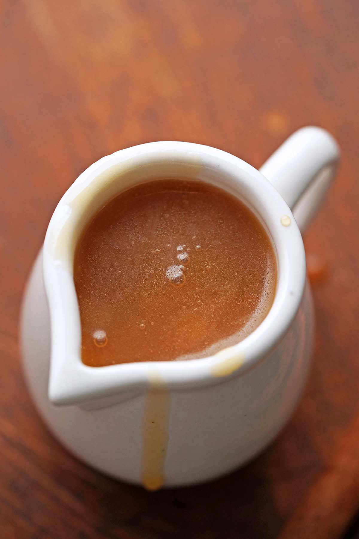 close up of homemade caramel syrup with apple cider in small white jug