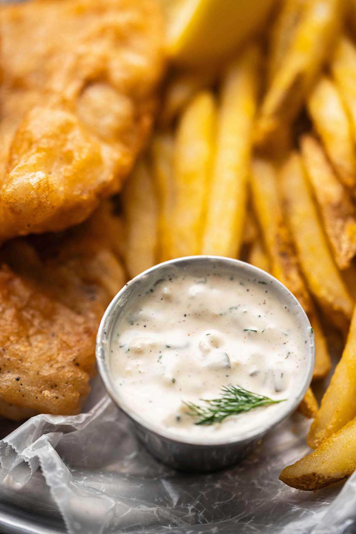dish of tartar sauce with fresh dill on plate with fish and chips