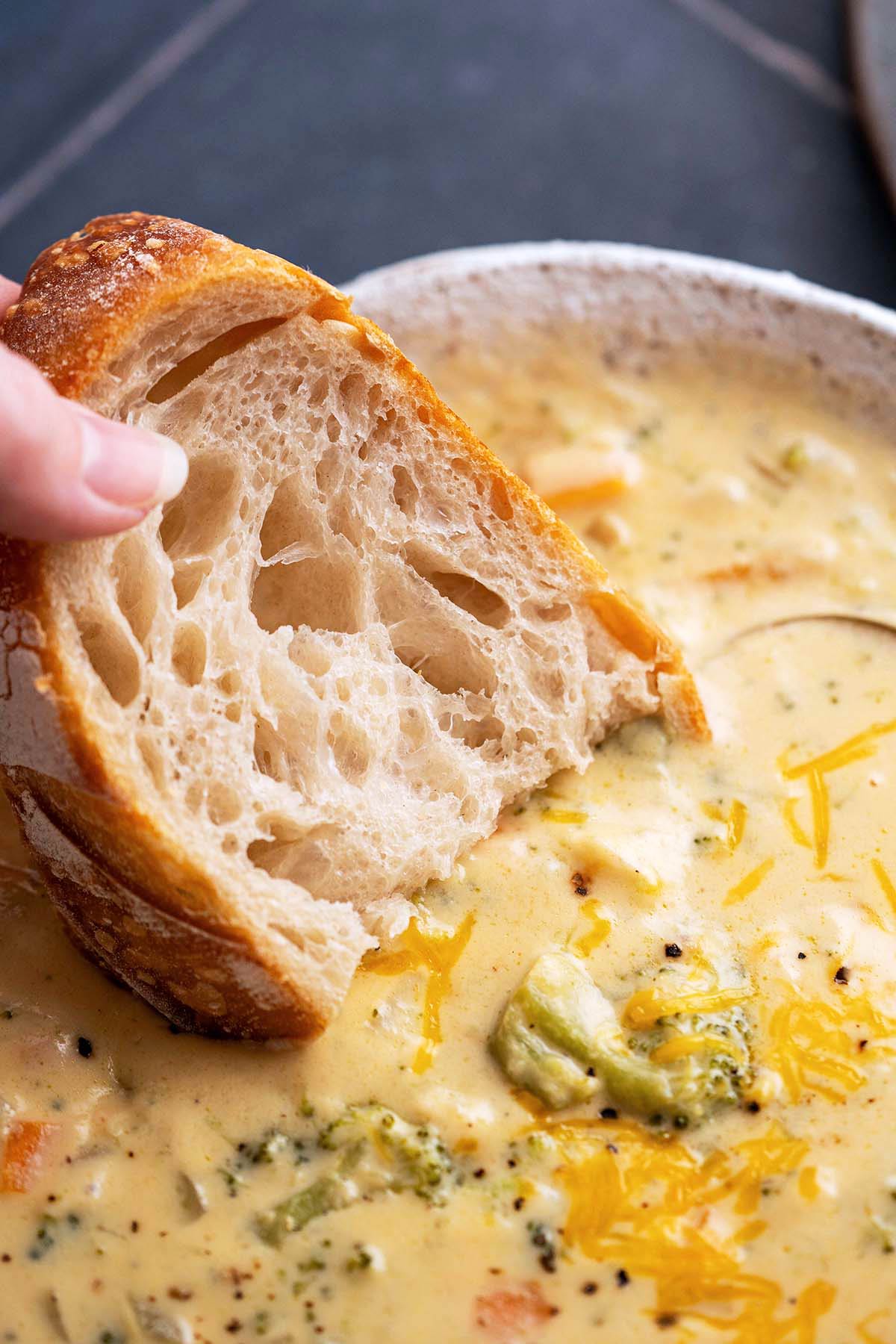 hand dipping pieces of sourdough bread into cream of broccoli cheddar cheese soup