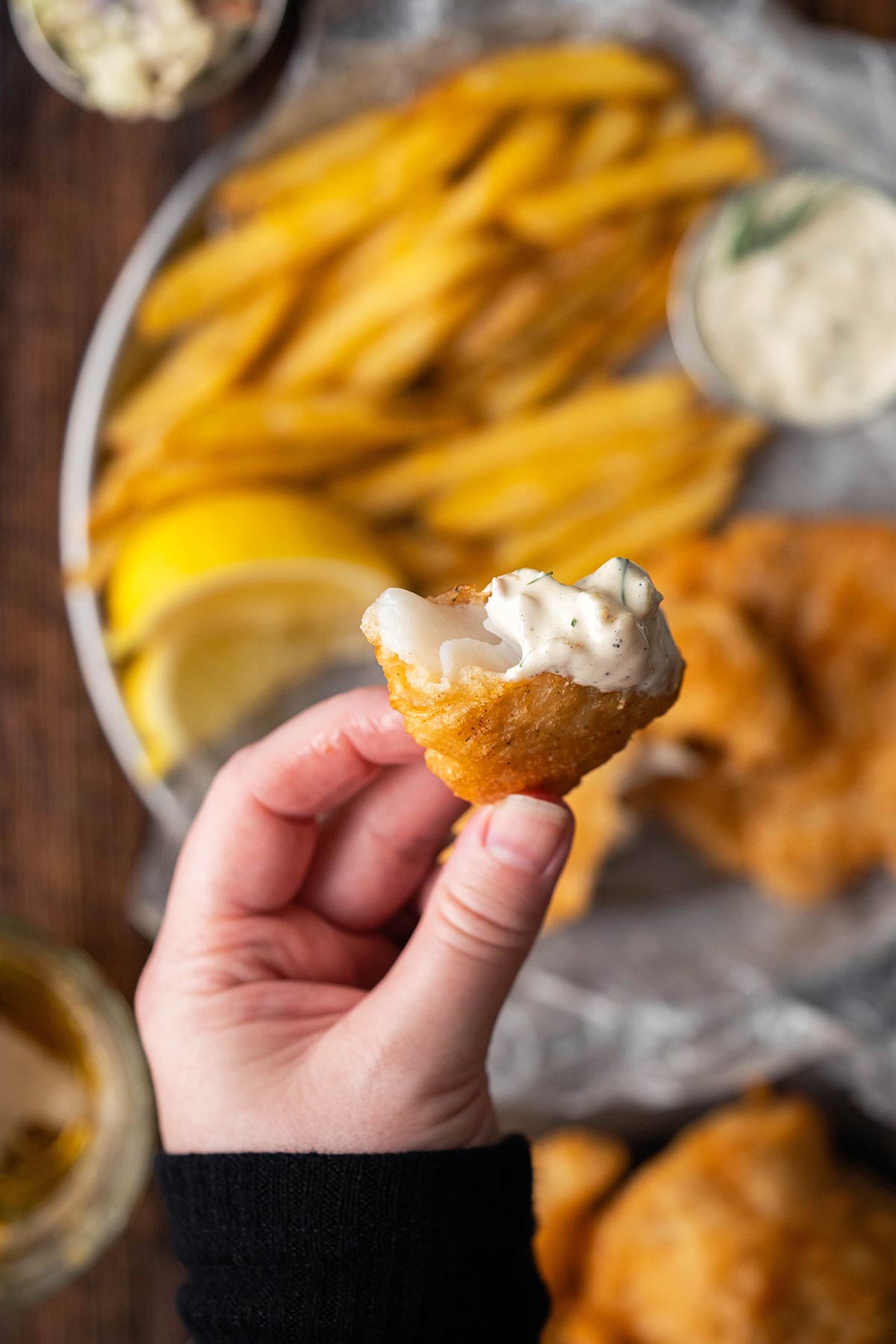hand holding flaky beer battered fish dipping in homemade tartar sauce