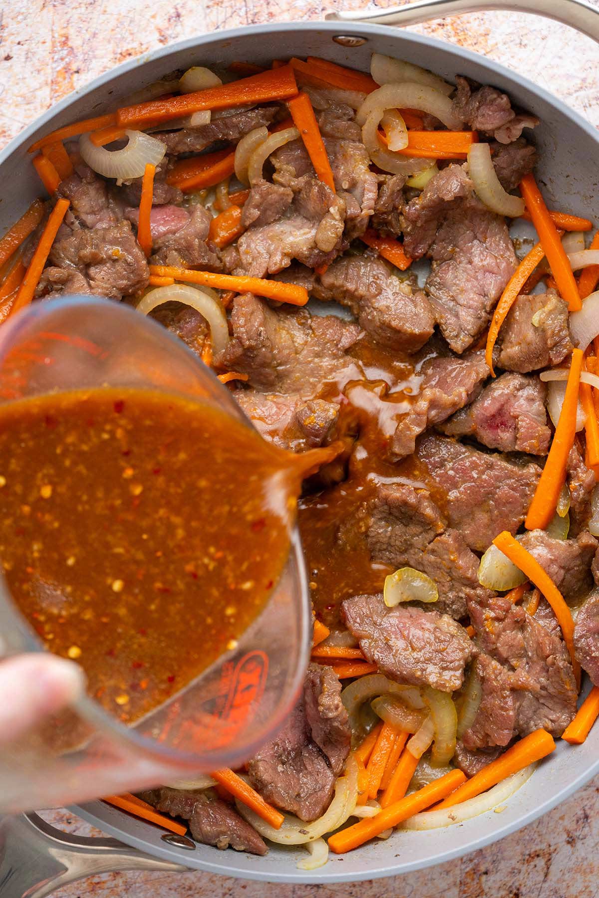 pouring homemade stir fry sauce into skillet of beef and vegetable stir fry