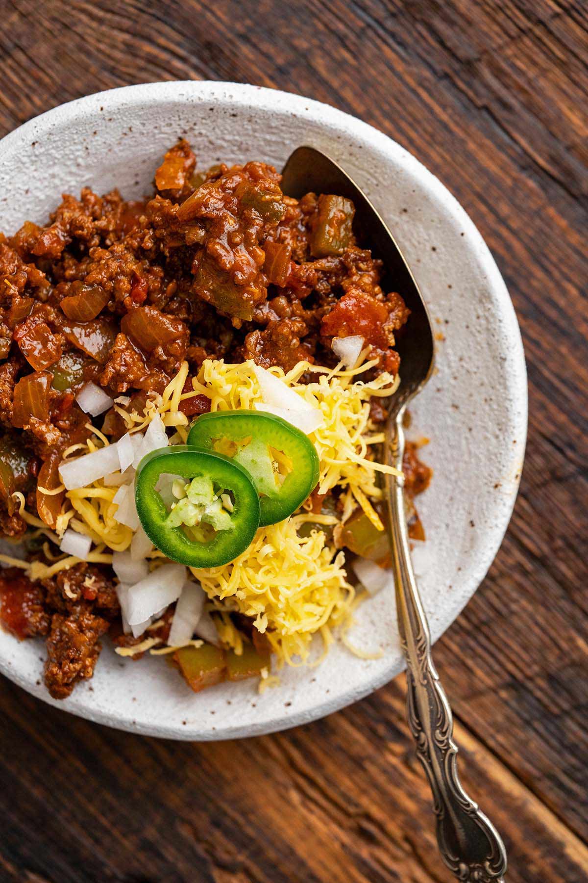 top view of chili without beans in stoneware bowl with cheese and toppings