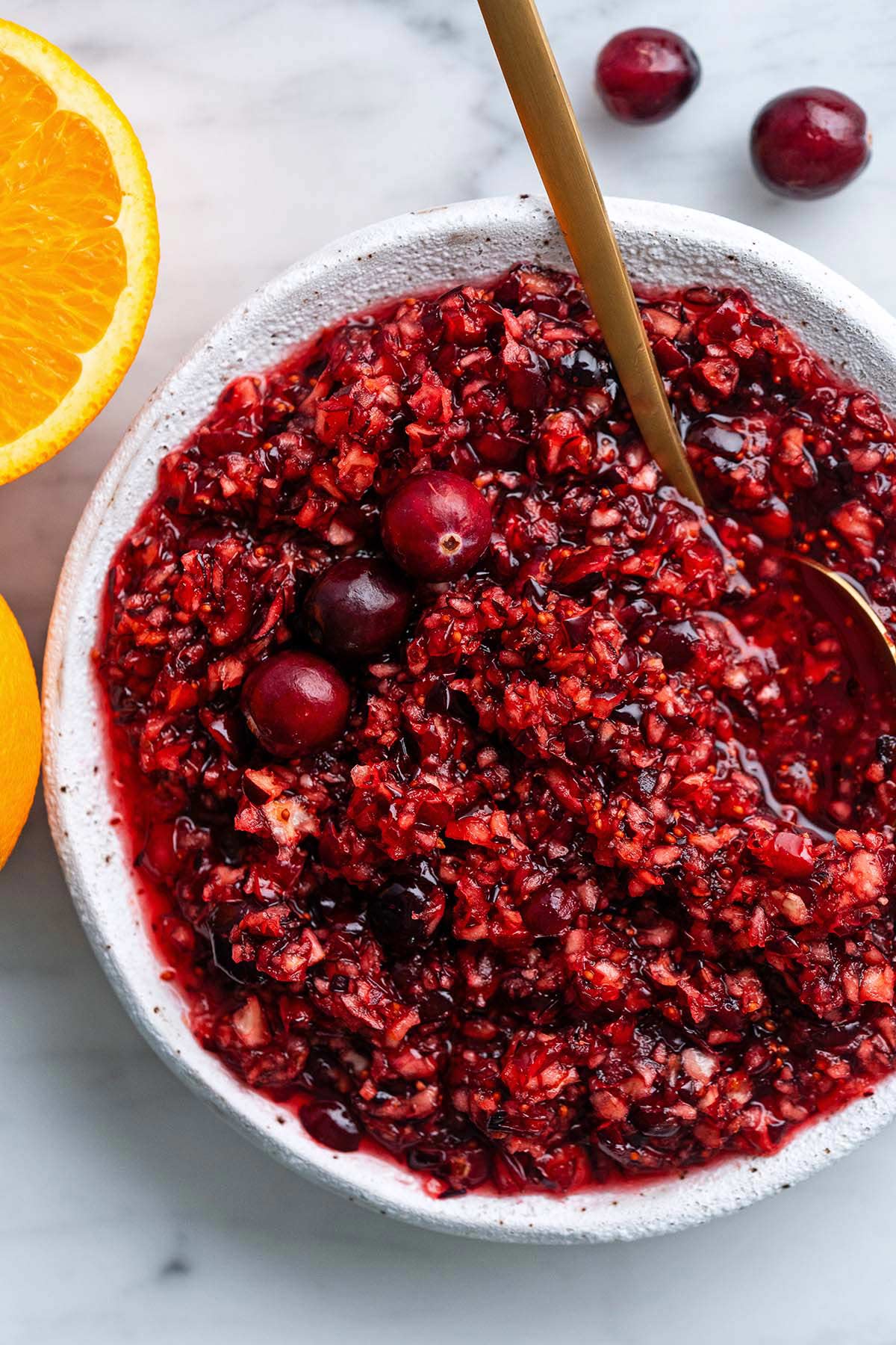 close up top view of raw cranberry orange relish in stoneware bowl on marble countertop