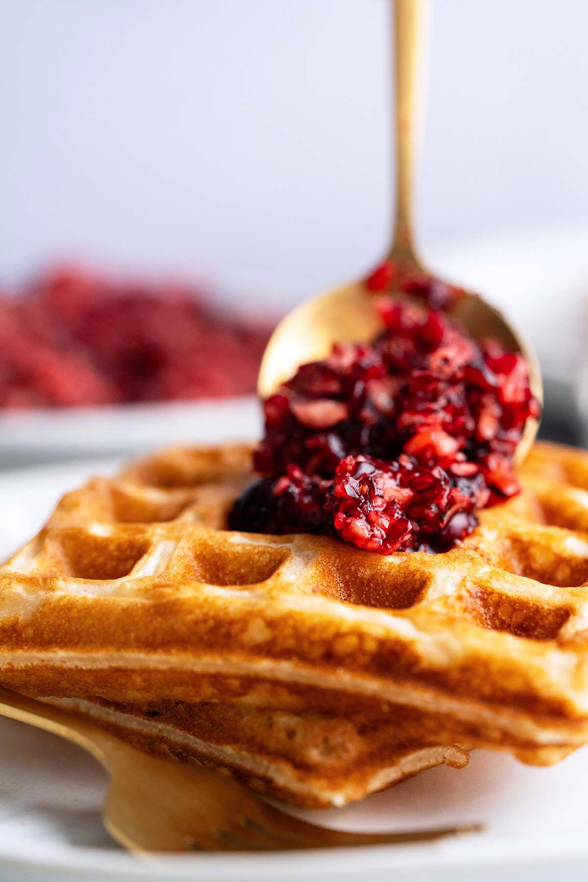 gold spoon adding cranberry relish on top of sourdough waffles