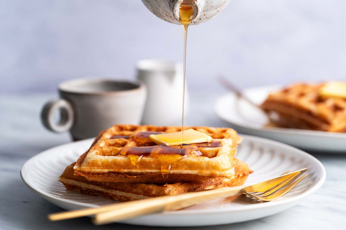 pouring maple syrup onto crispy waffles topped with butter