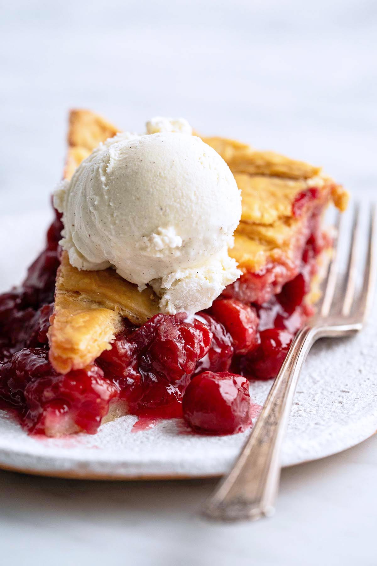slice of homemade tart cherry pie on stoneware plate topped with scoop of French vanilla ice cream