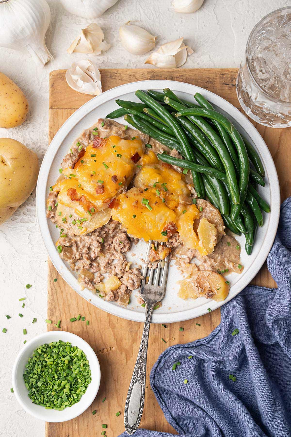 serving of cheesy hamburger potato casserole on plate partially eaten with green beans
