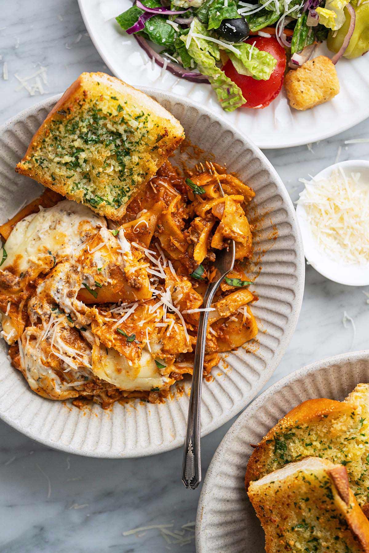 cheesy ground beef Italian lasagna made in dutch oven served with salad and garlic bread