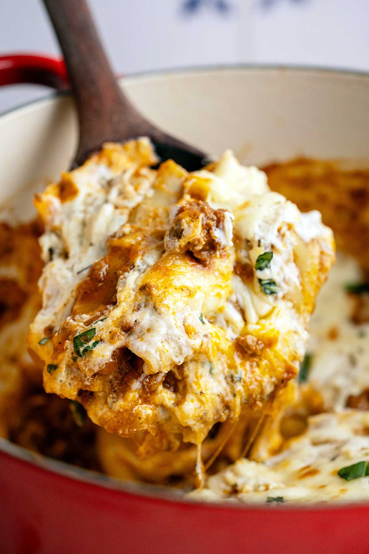 close up of serving spoon over pot of gooey cheesy ground beef lasagna