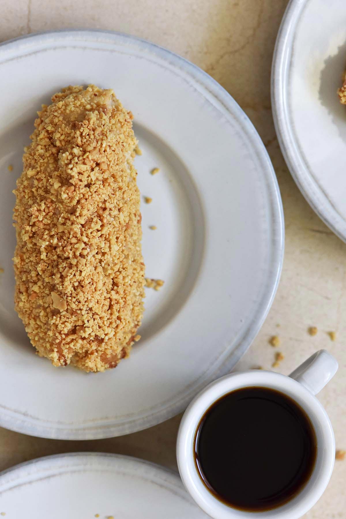 top view of buffalo peanut stick donut on white plate next to cup of coffee