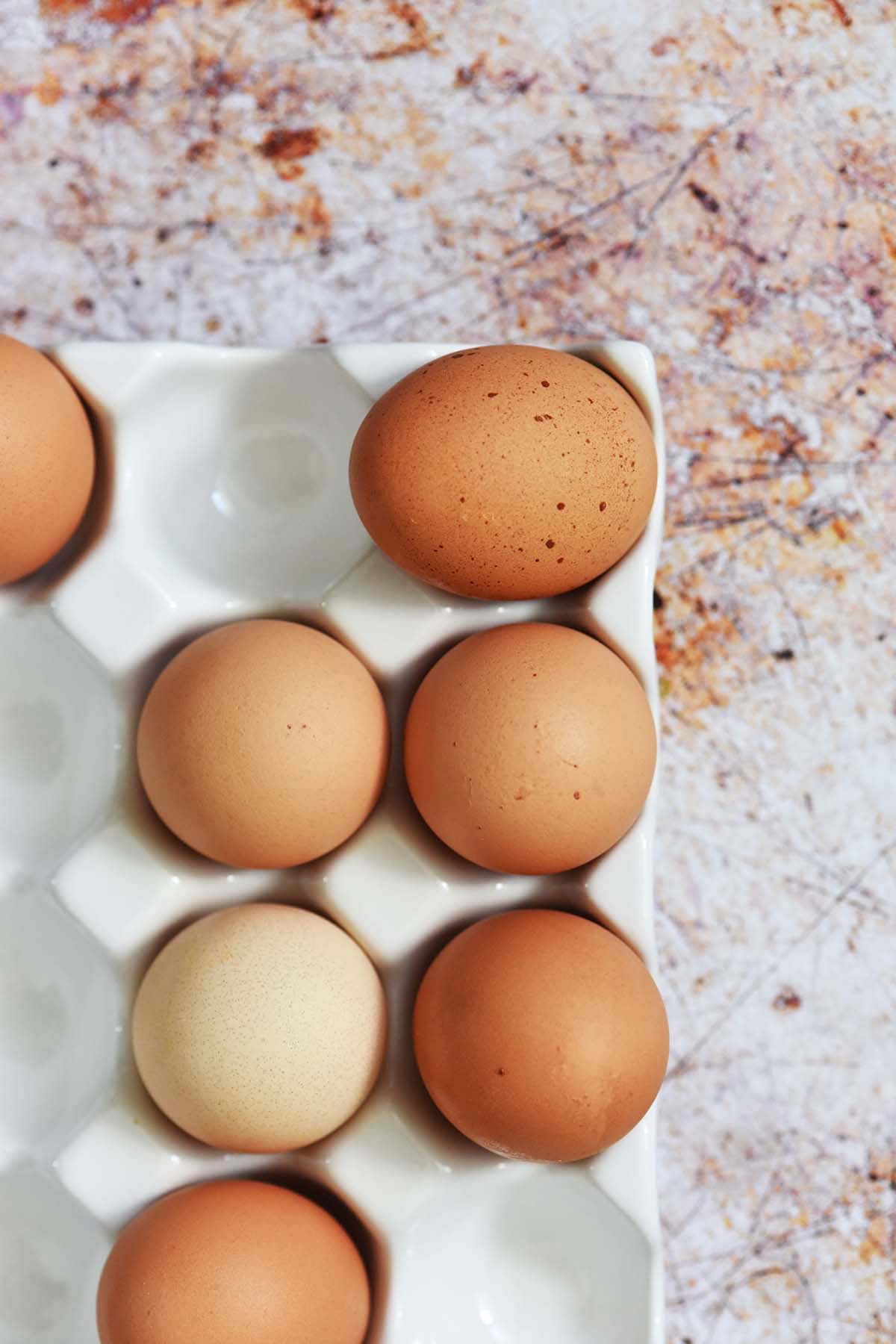 overhead view of speckled brown eggs on white egg crate