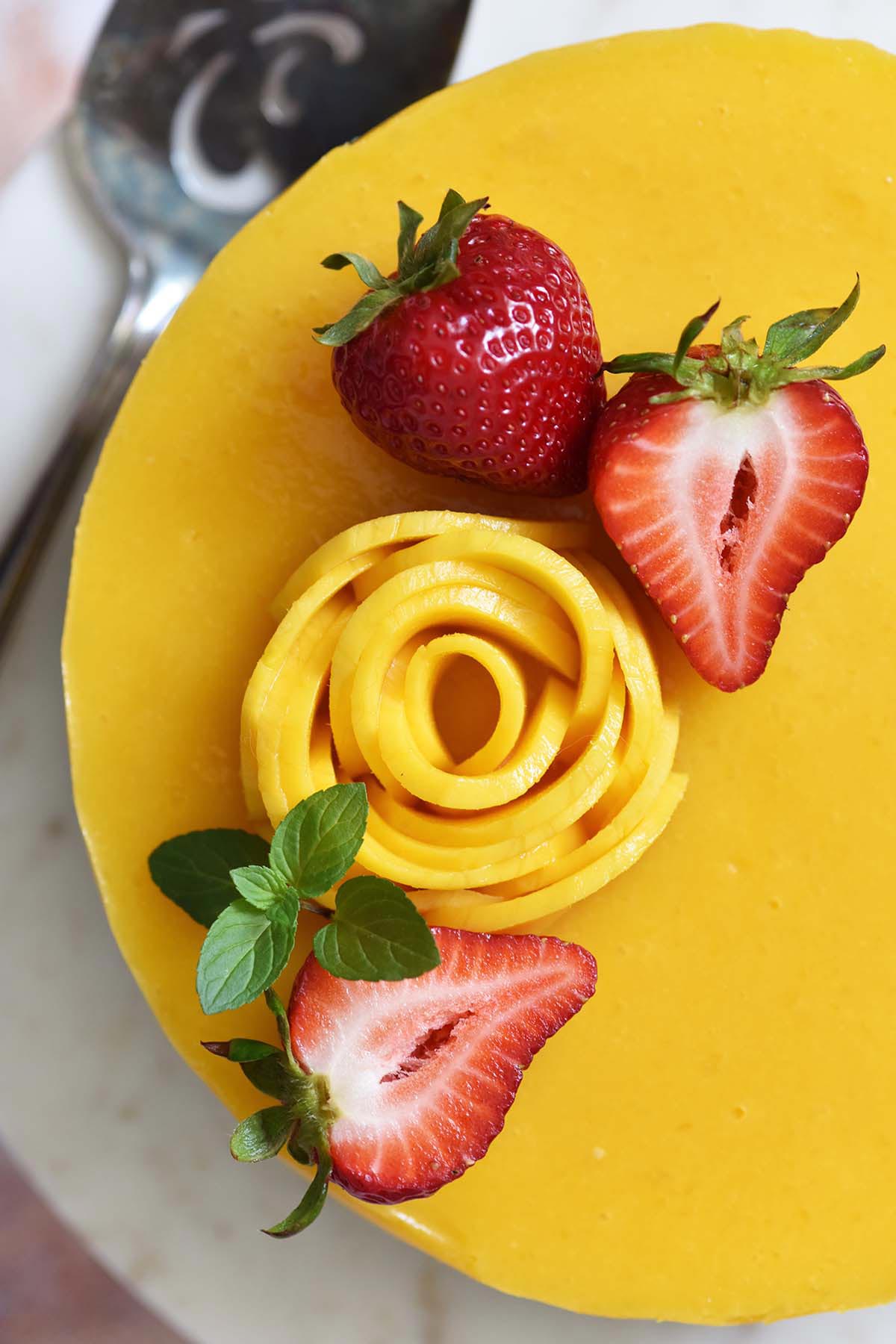 close up top view of fresh strawberries mango rose and mint on mango jelly cheesecake