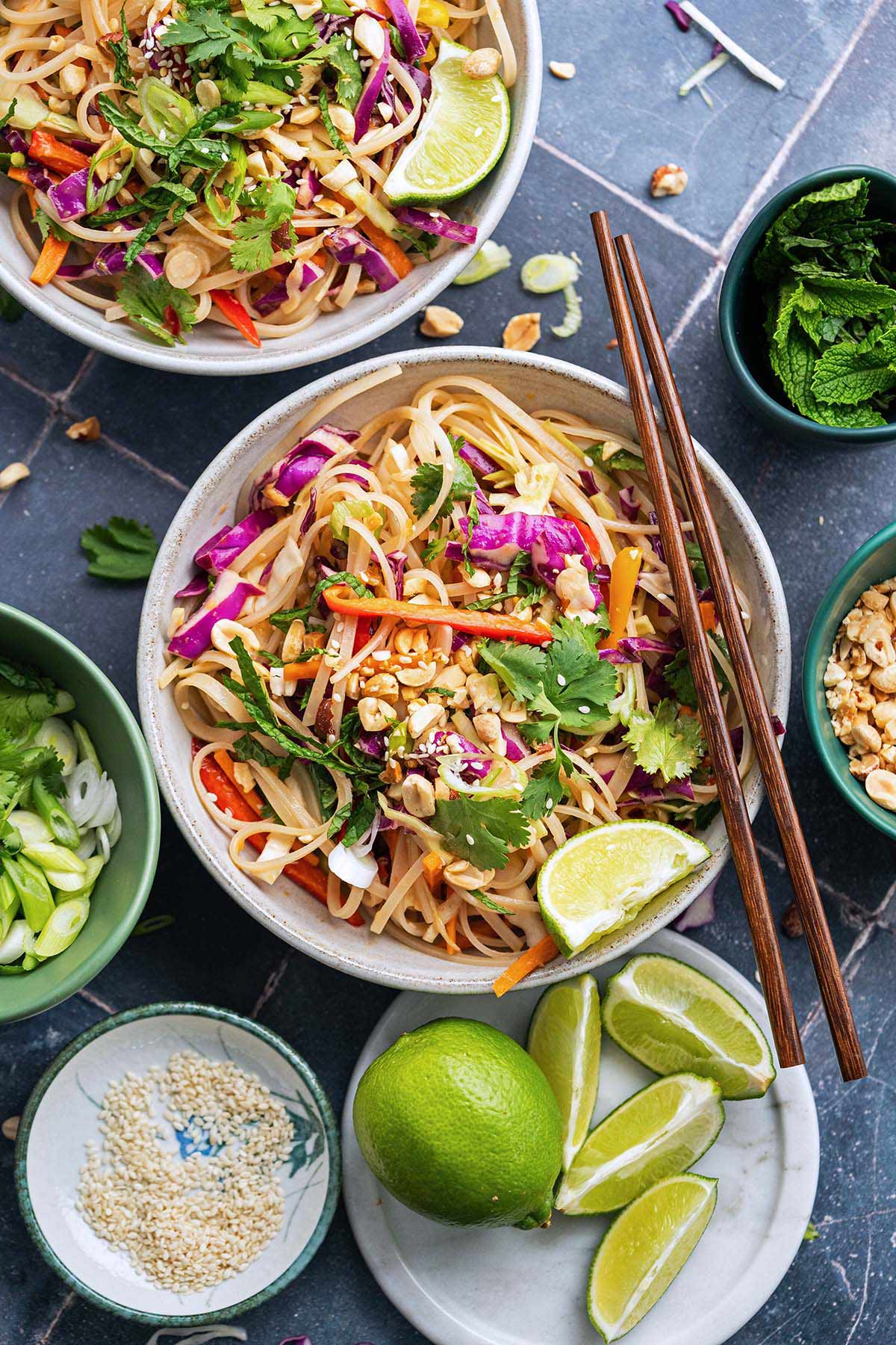 cold peanut noodle salad in stoneware dish with fresh herbs and lime garnish