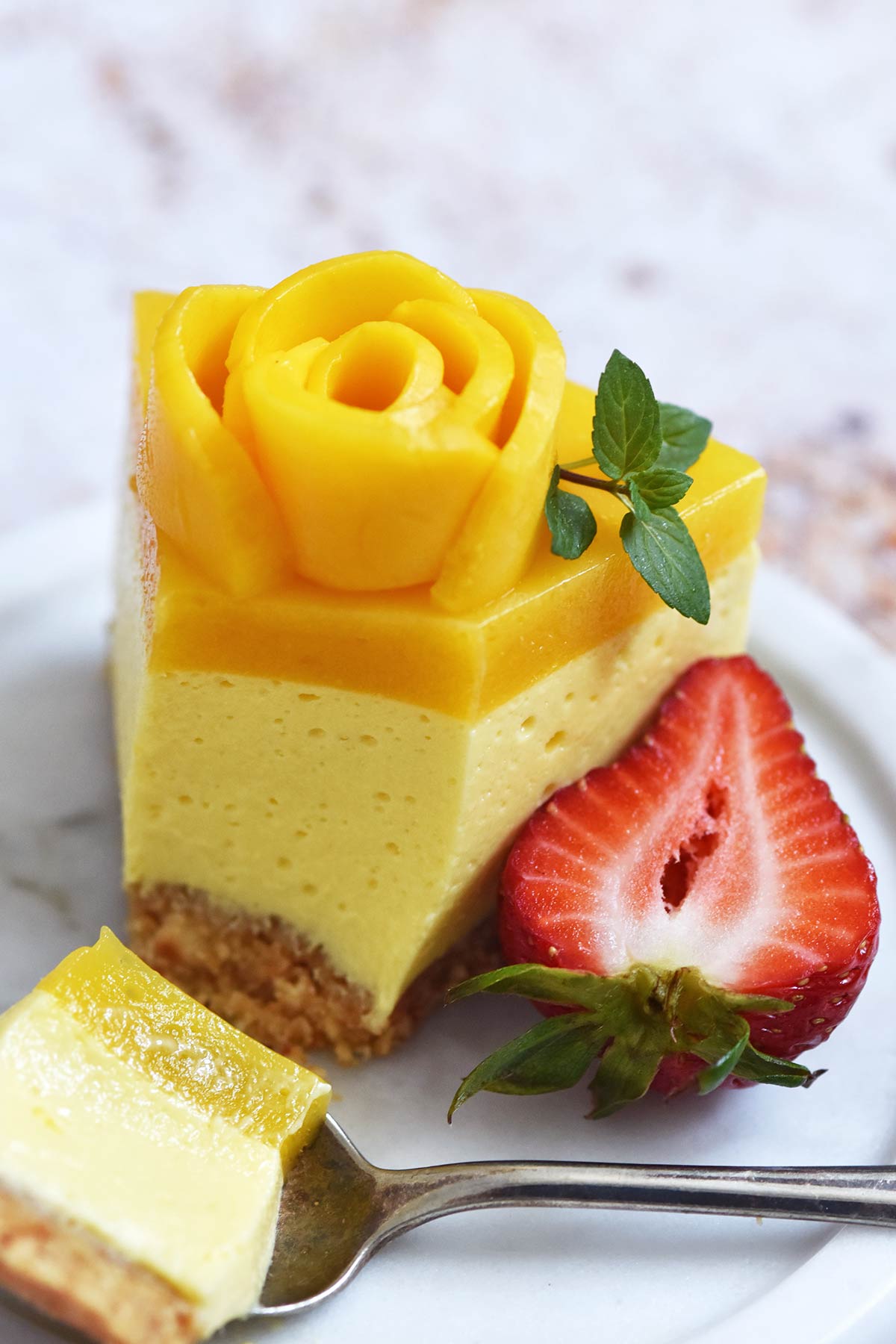 partially eaten slice of no bake cheesecake with mango rose and mango jelly topping showing layers