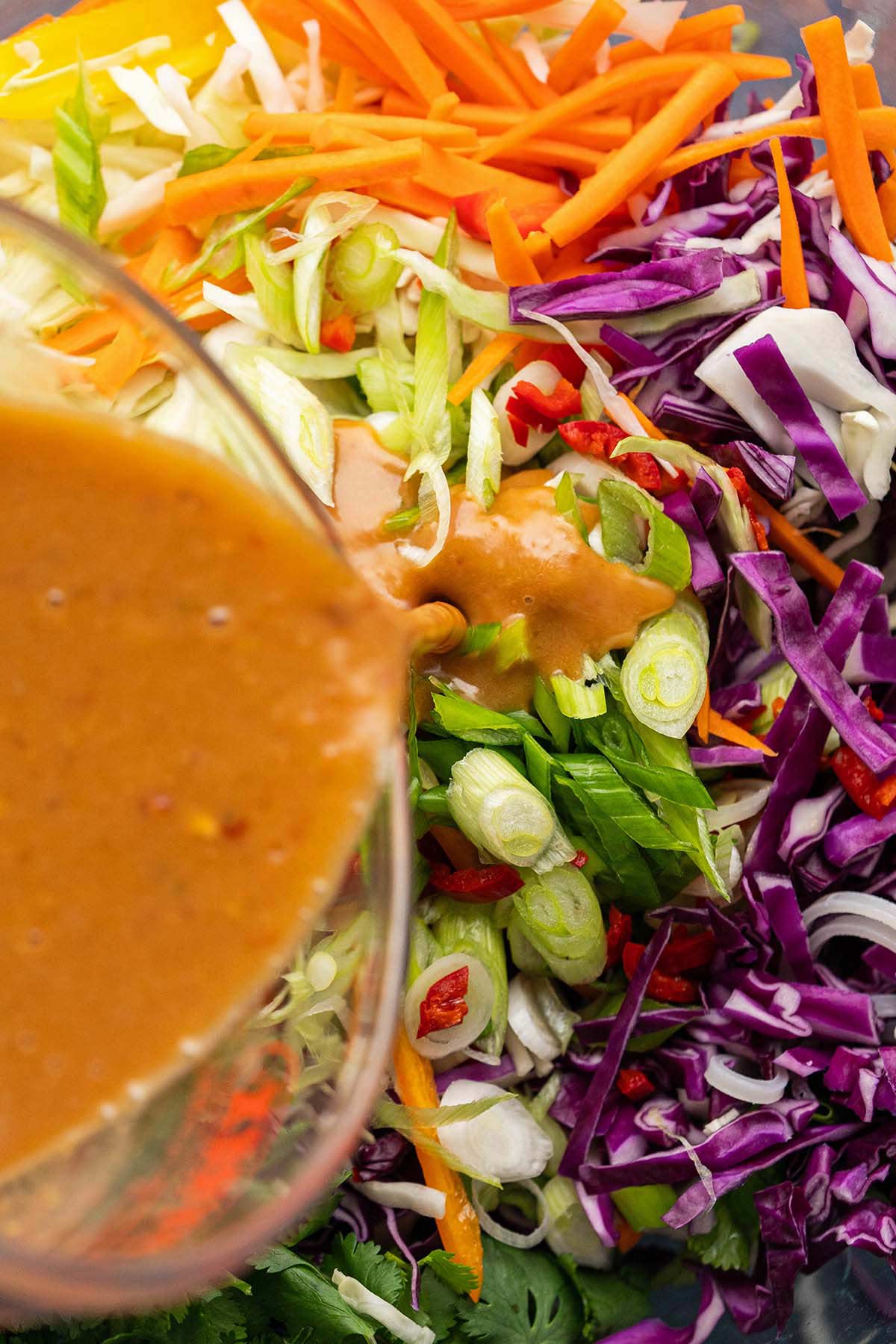 pouring thai peanut dressing on slaw salad