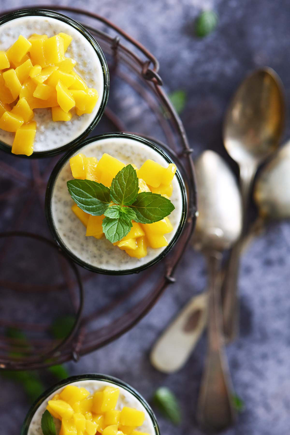 top view of coconut chia mango pudding in glasses with vintage spoons