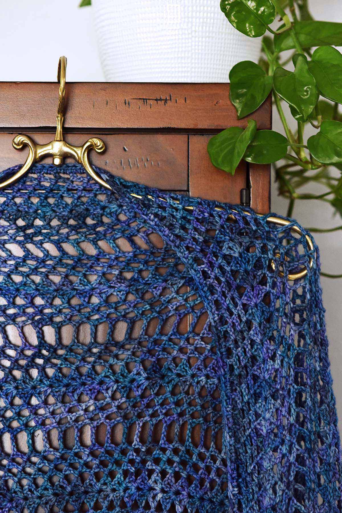 women's crochet shawl hanging on brass hanger
