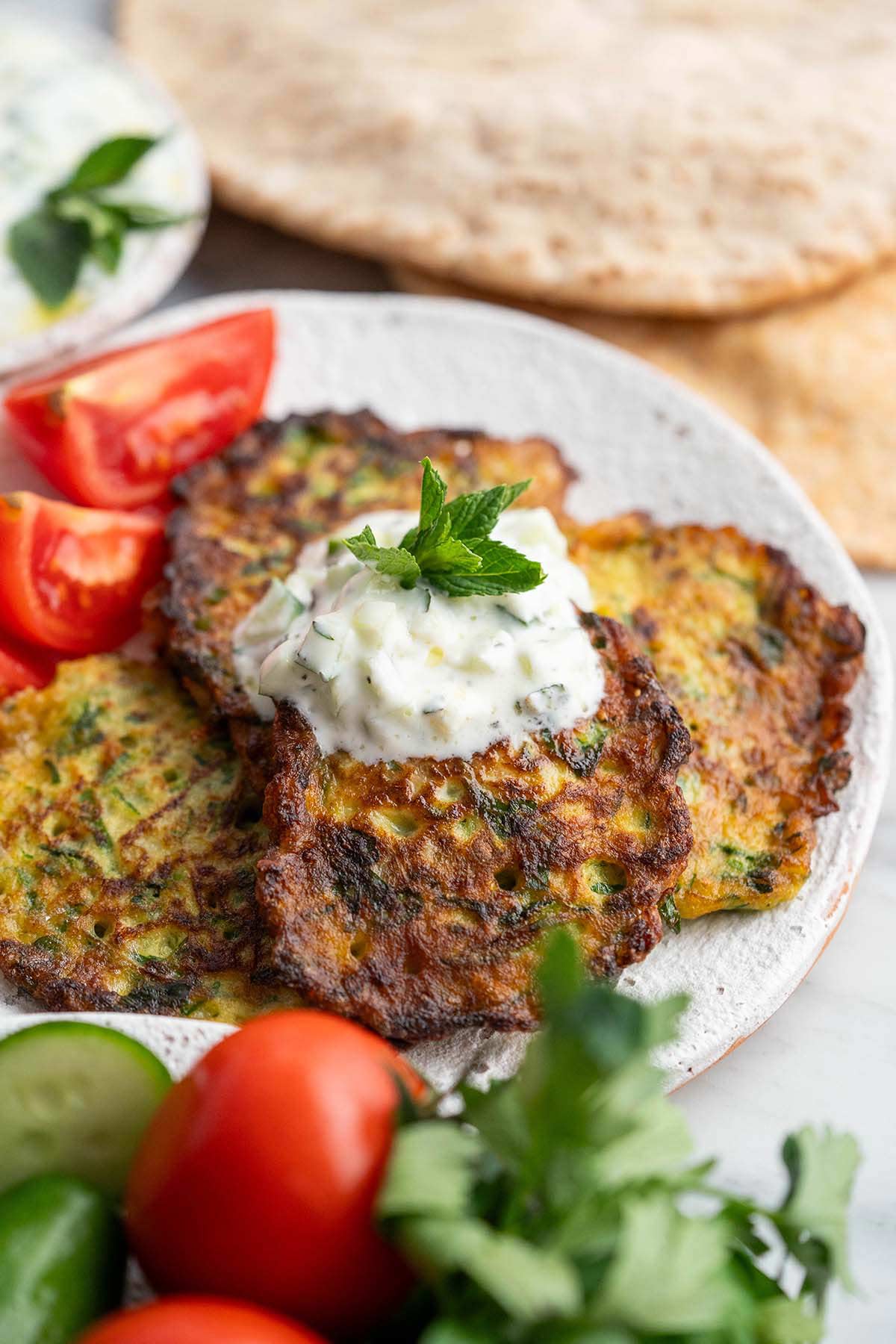 front view of pan fried zucchini fritters ejjet kousa topped with cucumber yogurt salad and mint