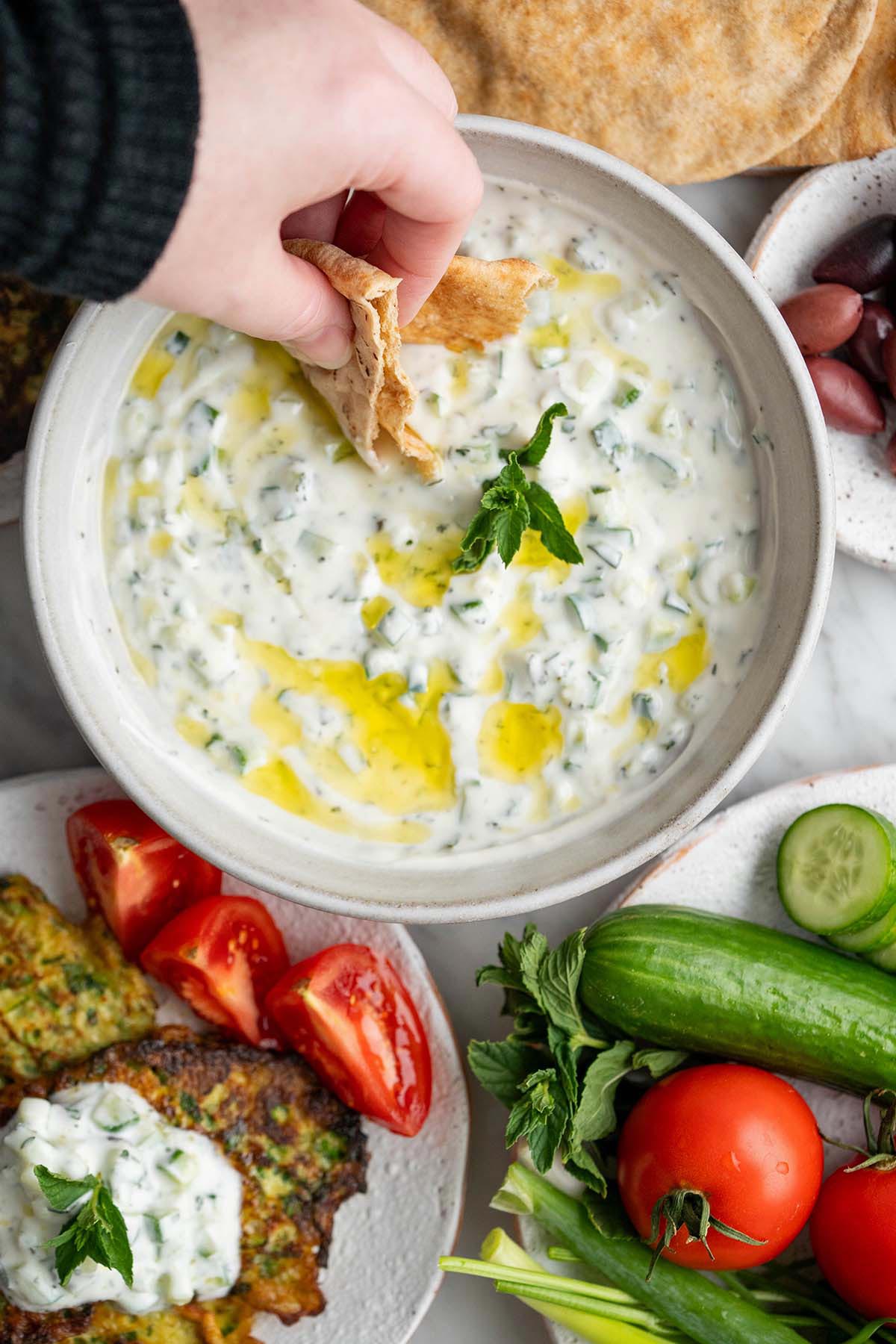 hand dipping arabic flatbread into cucumber yogurt salad with middle eastern breakfast ejjeh spread