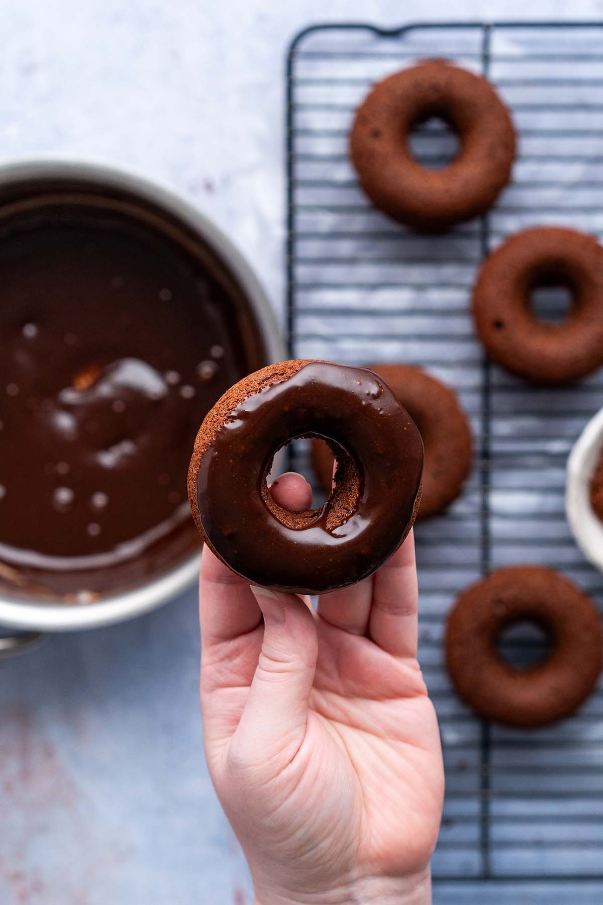hand holding baked chocolate doughnut dipped in chocolate glaze