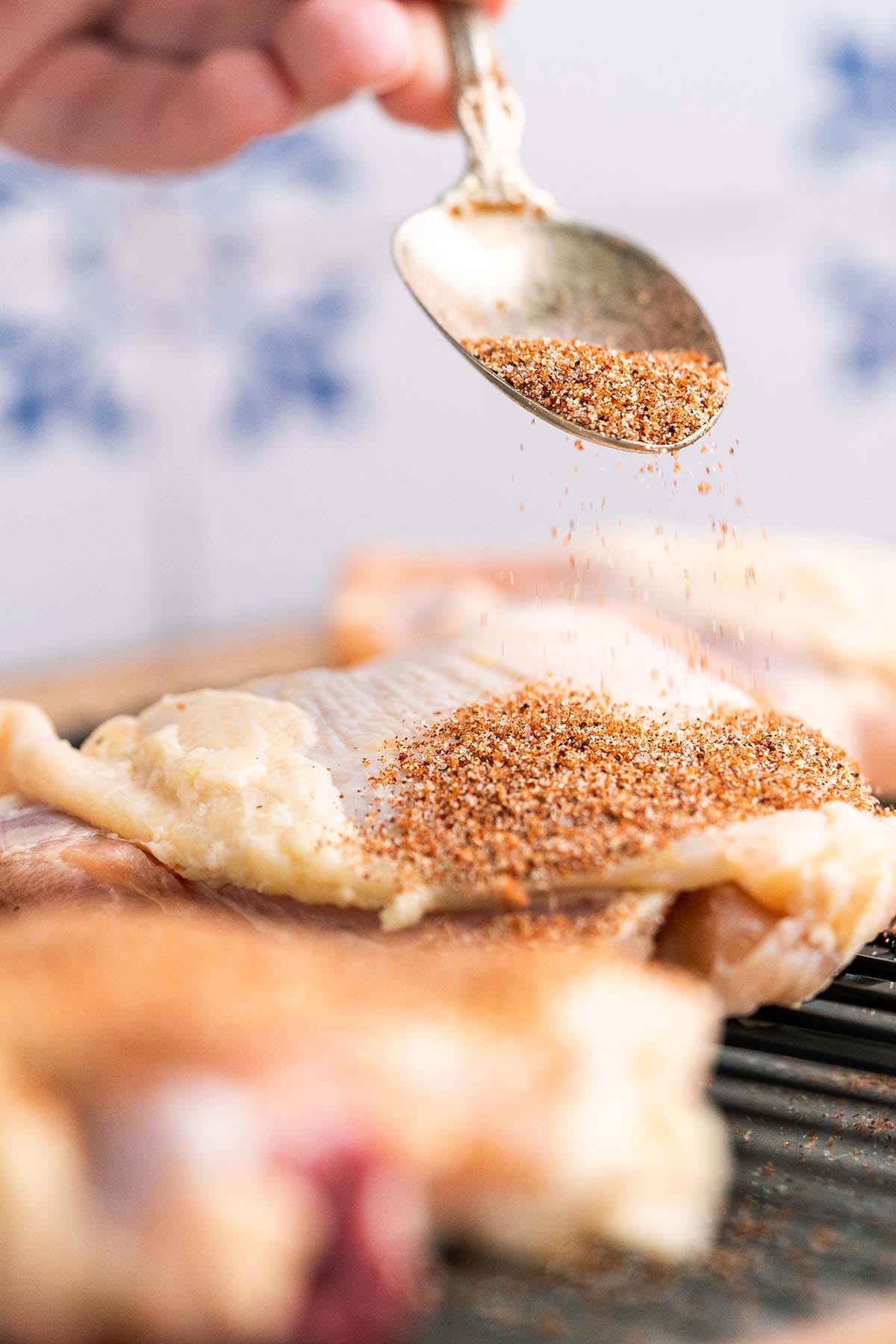 sprinkling bbq dry rub onto chicken thighs