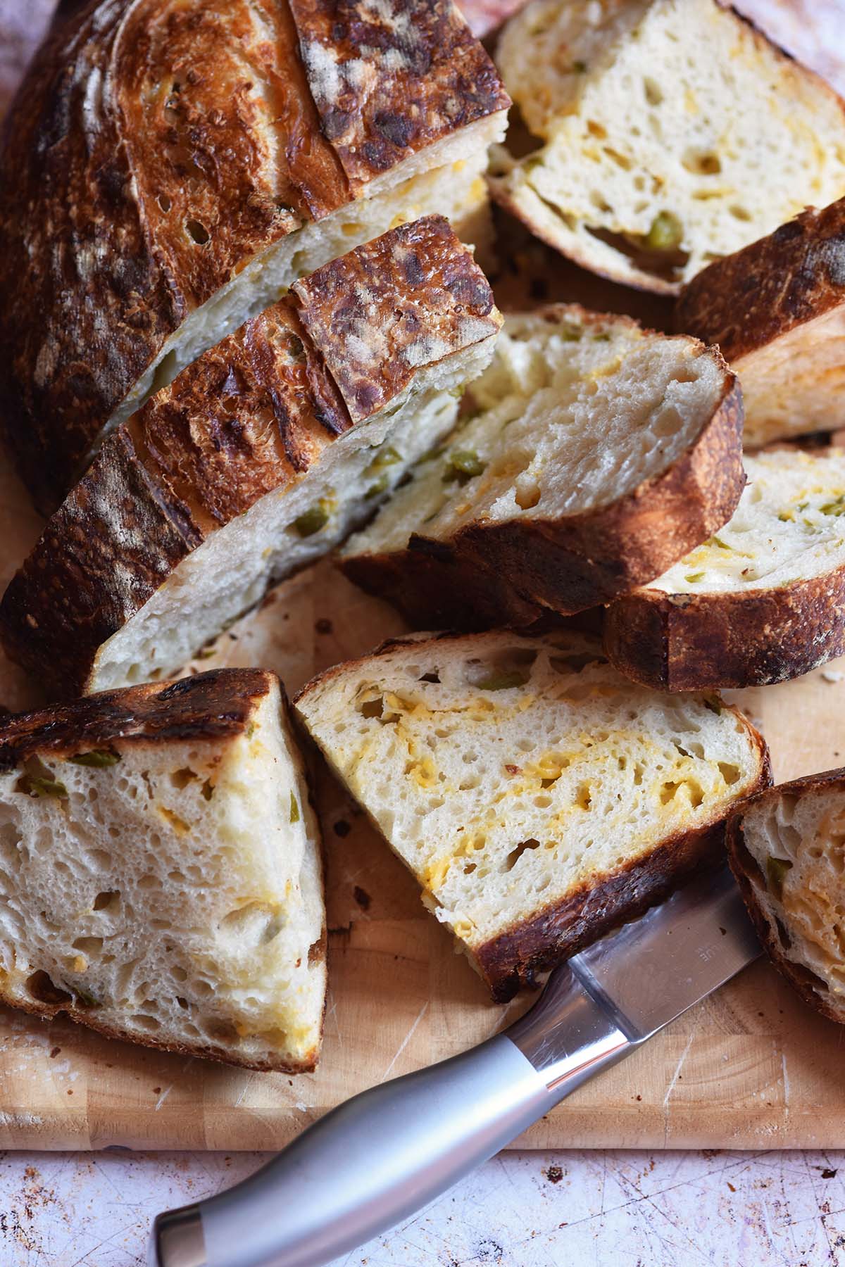 pile of sliced jalapeno cheddar sourdough loaf on cutting board with bread knife