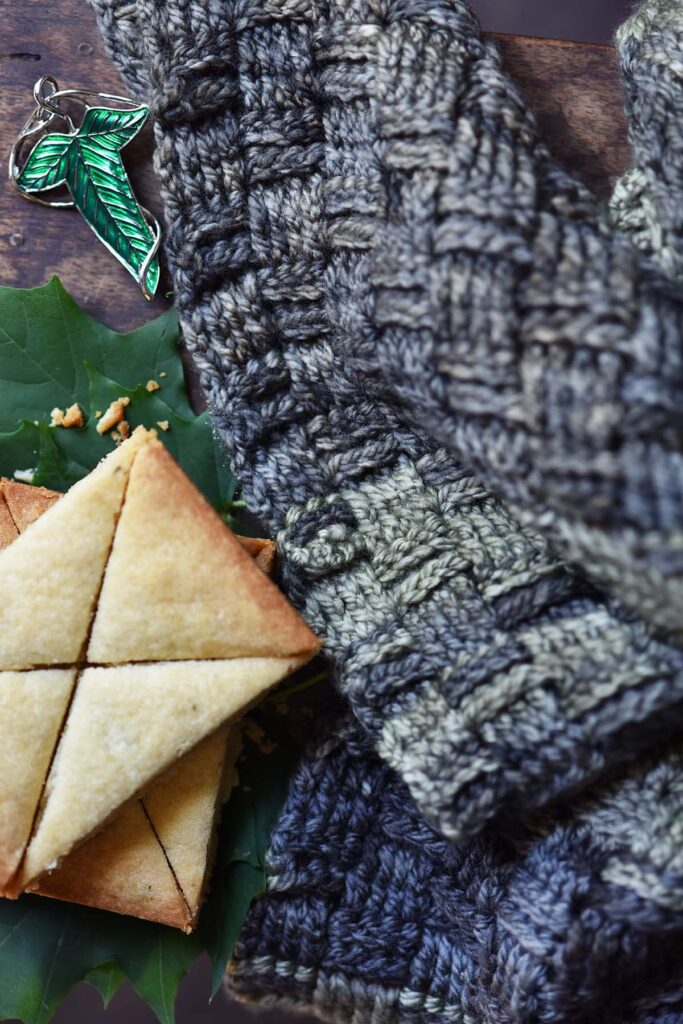 basketweave crochet shawl inspired by lotr fellowship cloak next to leaves of Lorien pin and lembas bread